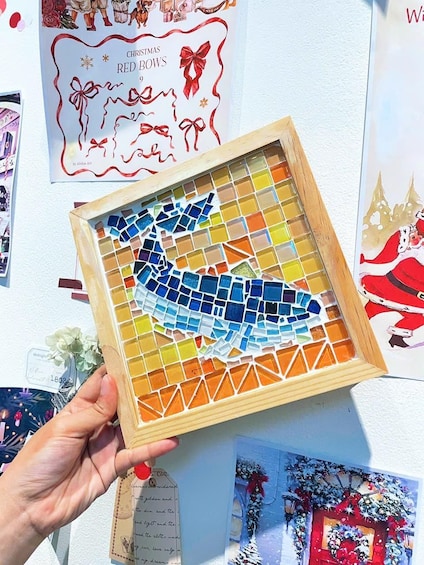 Un mosaico de un pájaro en marco de madera, sostenido por una mano. 2