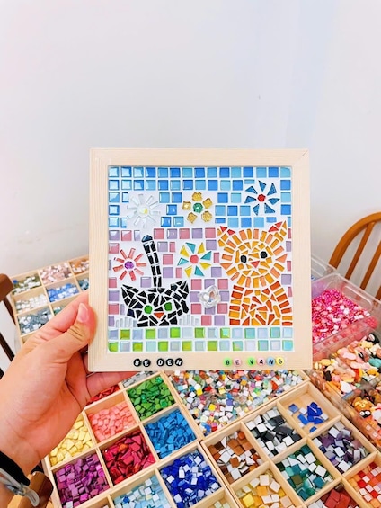 Una mano sostiene un tablero de mosaico con baldosas coloridas que representan animales. 3