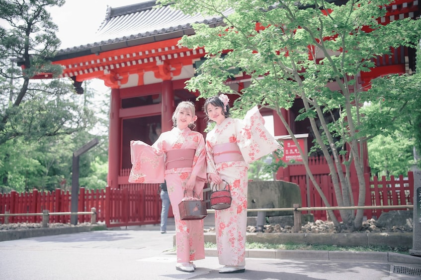 Two individuals in traditional Japanese attire standing in front of a red building with a tiled roof. 1
