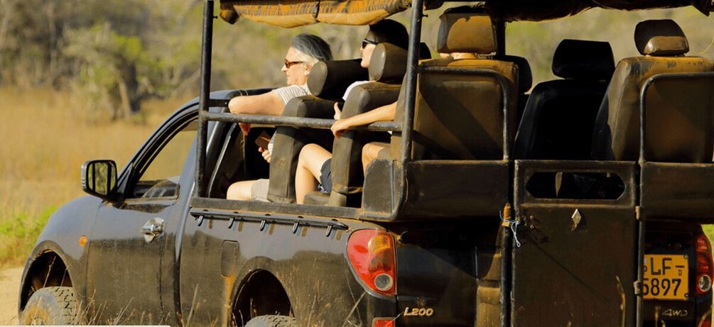 A safari vehicle with two passengers, a man and a woman, driving through a grassy area. 1