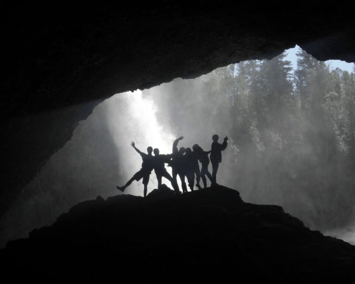 A group of people standing on a rock formation inside a cave with sunlight filtering through. 3