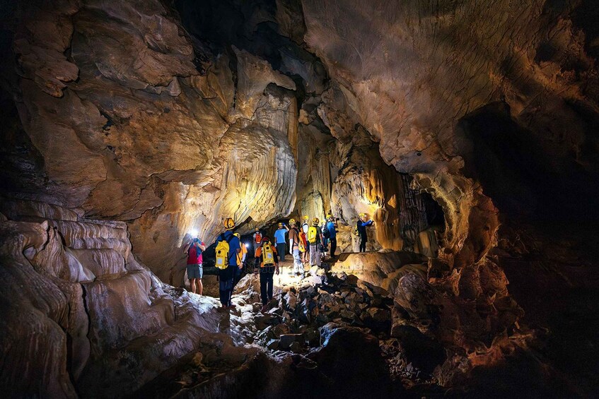 A group of people exploring a cave with rugged rock formations and a narrow passageway. 3
