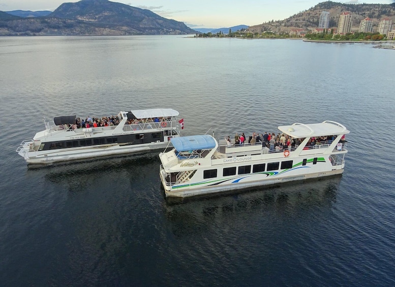 Two white tour boats on a calm lake with passengers, surrounded by hills and buildings. 1