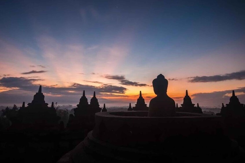 A silhouette of a large Buddha statue against a sunset sky, surrounded by smaller temple structures. 2