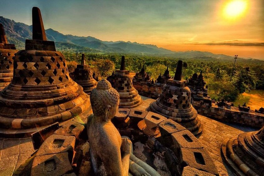 Ancient stone structures with a Buddha statue in the foreground, set against a mountainous backdrop during sunset. 4
