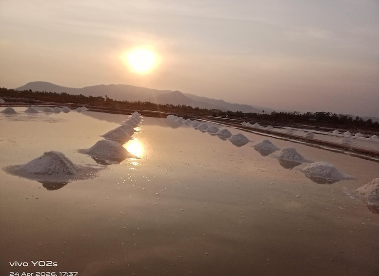 A salt flat with piles of salt and mountains in the background during sunset. 5