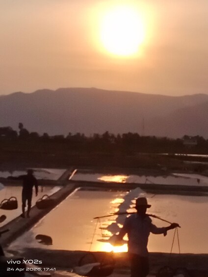 A person fishing at sunset with a boat on a calm water body, surrounded by mountains. 4