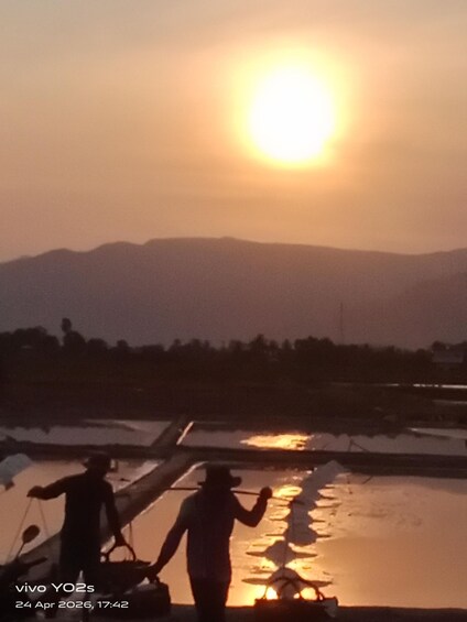 A sunset over a body of water with silhouettes of people and a boat. 2