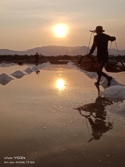 A person walking on a reflective surface with the sun low on the horizon, casting a warm glow. 1