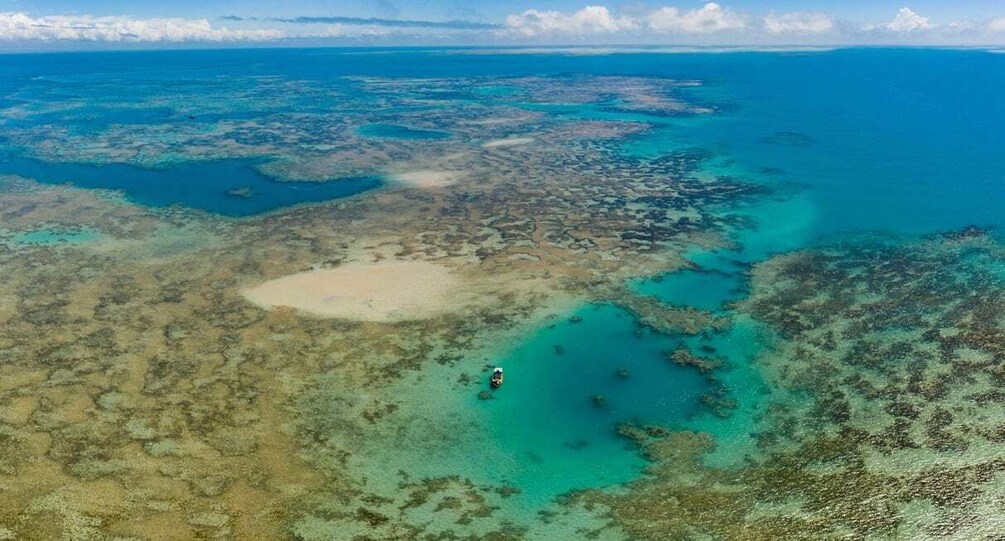 An aerial view of a coastal area with clear blue waters, a sandy beach, and a boat in the distance. 5