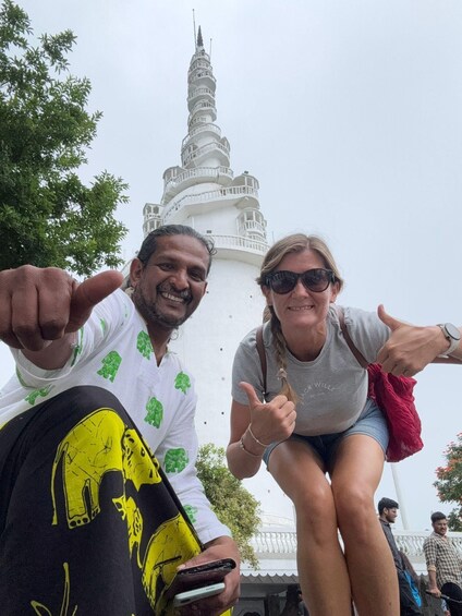 Two people giving thumbs up in front of a white tower with balconies. 1