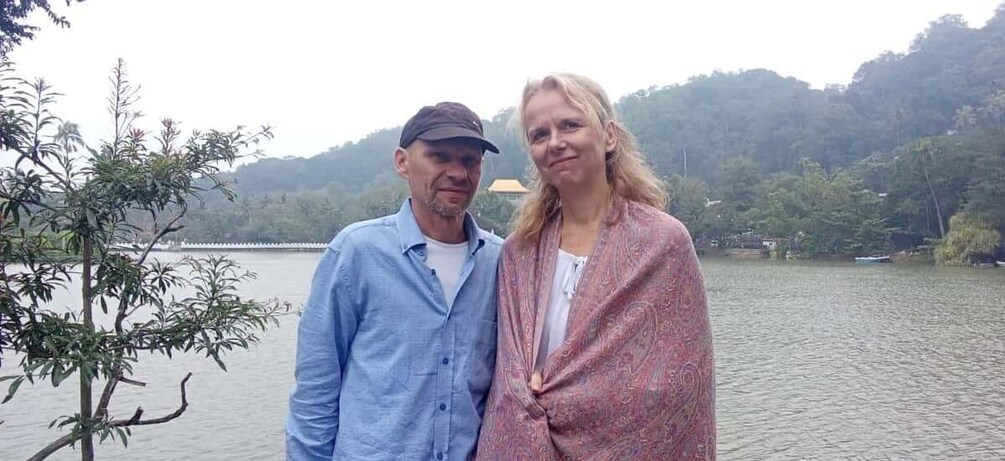 Two people standing by a lake with a tree and hills in the background. 4