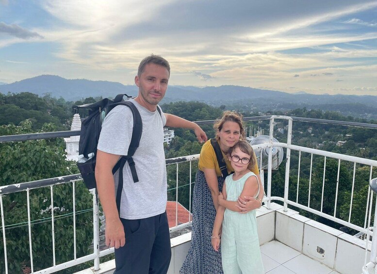 A man and two children on a balcony with a scenic view of mountains and greenery. 5