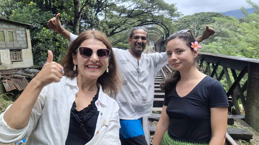 Three people standing on a bridge with greenery in the background. 3
