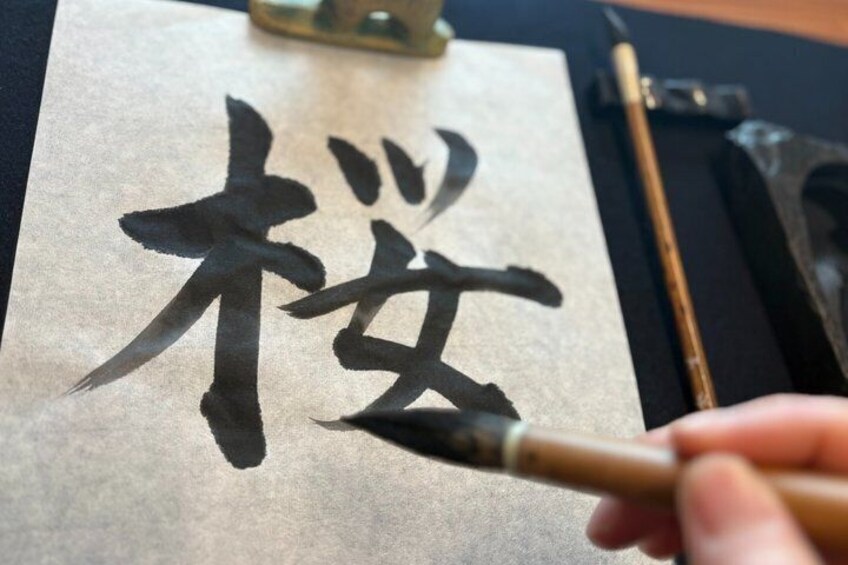 A hand holding a brush, painting Chinese calligraphy on paper. 1
