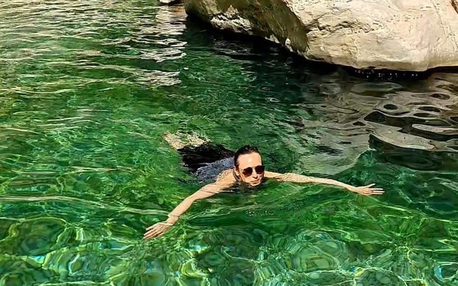 A person swimming in clear water with rocks in the background. 3