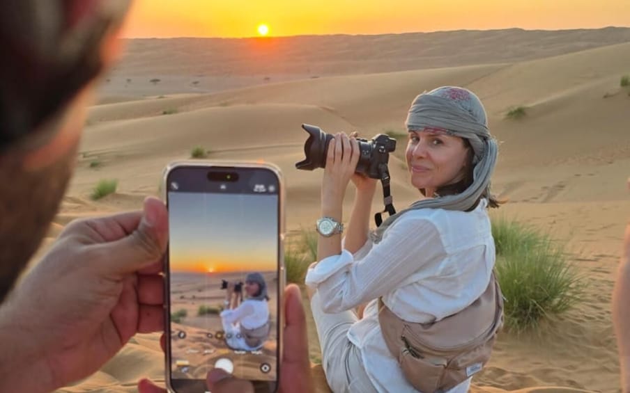 A person taking a photo with a camera in a desert landscape at sunset. 3