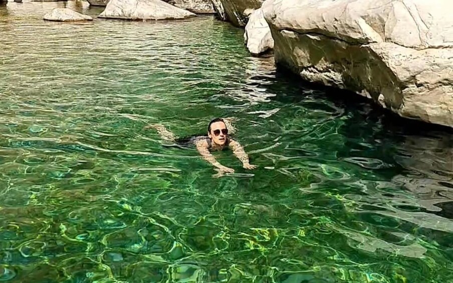 A person swimming in clear water with rocks in the background. 2