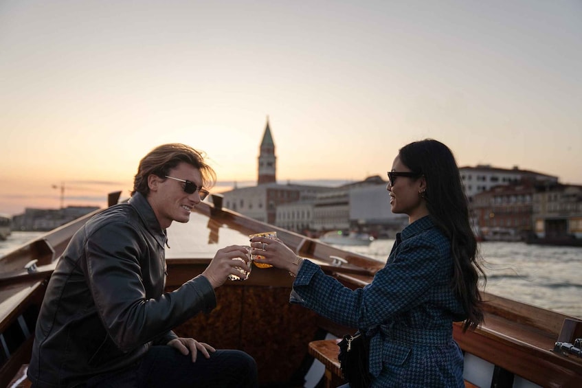 Two people sitting on a boat, holding glasses, with a cityscape and a tower in the background. 5
