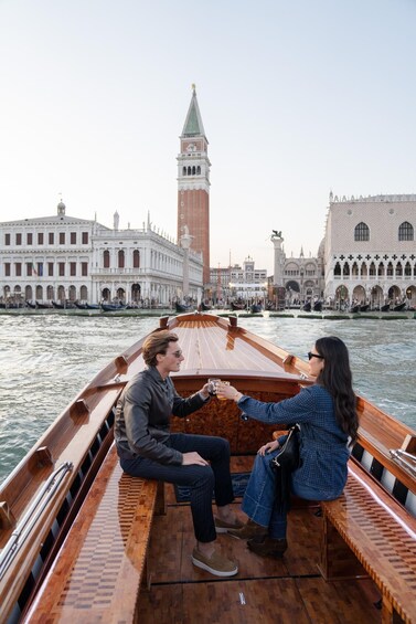 A boat with two people sitting on the deck, a clock tower, and historic buildings in Venice. 3