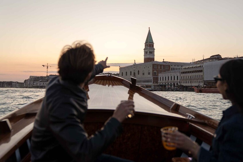A boat with two people, one pointing towards a historic building with a tower, likely St. Mark's Basilica, in Venice. 4