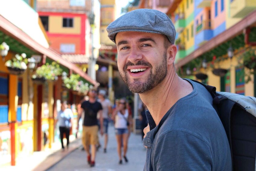 A man in a grey shirt and cap walking down a colorful street with buildings on either side. 1