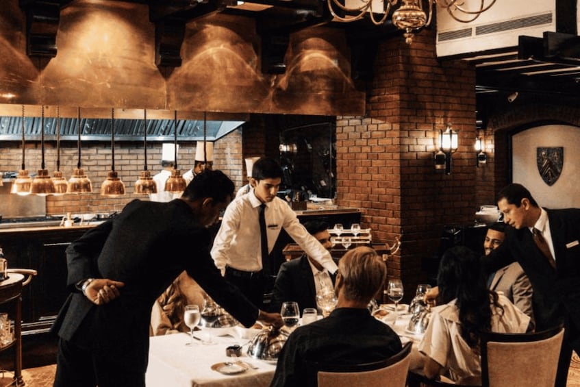 A restaurant interior with brick walls, hanging copper pots, and a dining area with patrons and waitstaff. 3