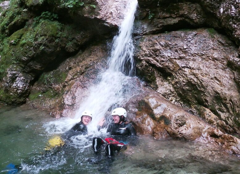 Two people in wetsuits and helmets near a waterfall in a rocky area. 4