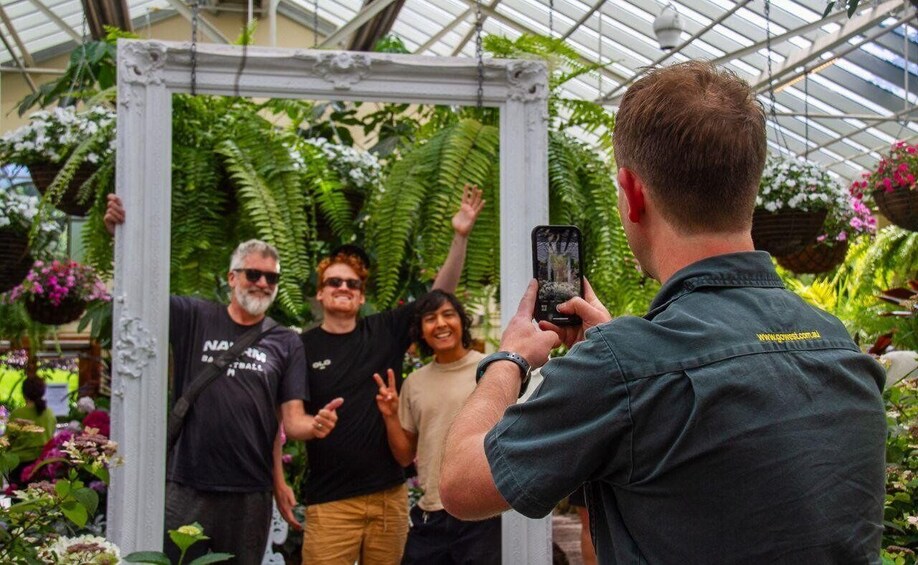 People taking a photo in a greenhouse with plants and a white frame structure. 5
