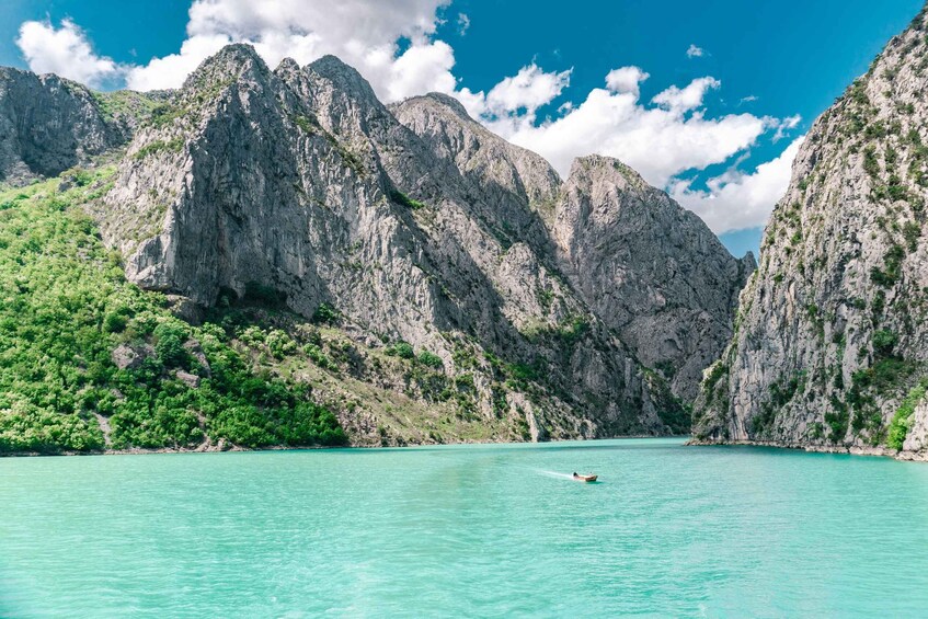 A turquoise sea with a boat, surrounded by rocky cliffs and green vegetation. 1