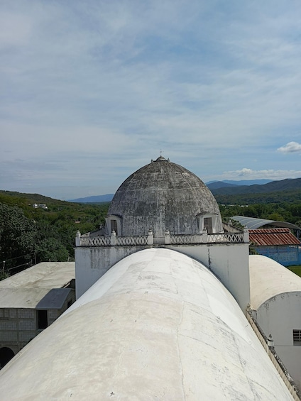 A dome structure atop a building with a flat roof, surrounded by greenery and distant mountains. 5