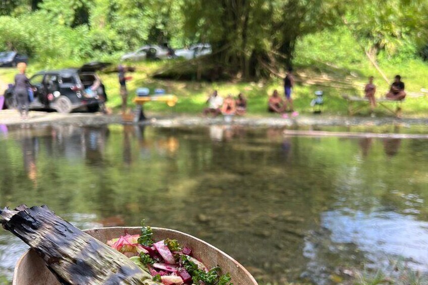 A bowl of salad with a fork in the foreground, a pond, and people in the background. 4