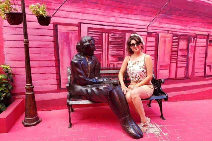 Une personne assise sur un banc, à côté d’une statue, dans un décor d’un rose vif. 3