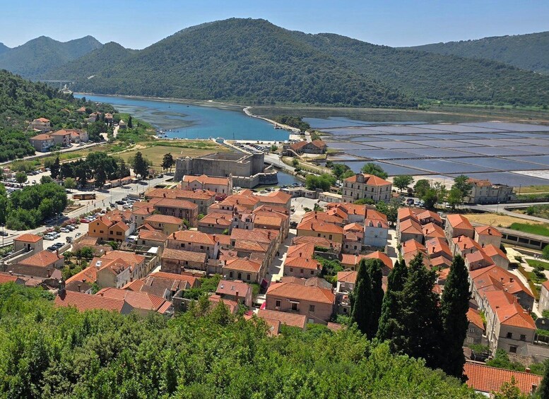 A coastal town with red-roofed buildings, a large body of water, and mountains in the background. 2