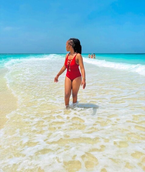 A person in a red swimsuit walking on a sandy beach with clear turquoise water. 3