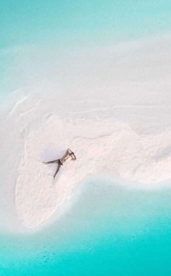 A person lying on a sandy beach with clear turquoise water. 2