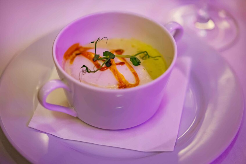A white cup of soup with a drizzle of sauce and a garnish on a white saucer. 5