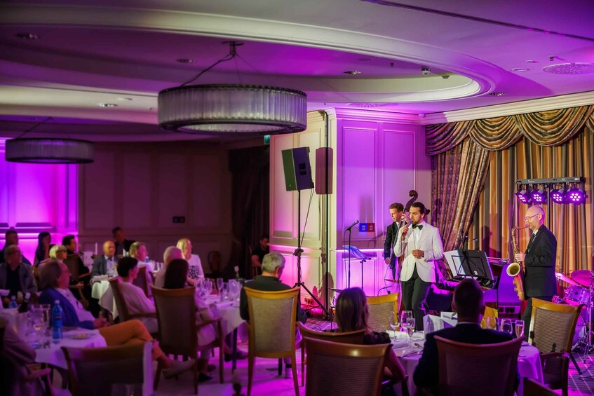 A formal event with a seated audience, a stage with a band, and a man speaking into a microphone. 2