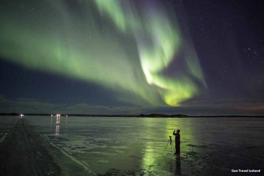 The Northern Lights over a frozen landscape with a tripod and a person observing. 1