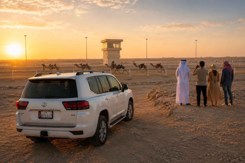 A white SUV parked on a dirt road with camels and riders in the background, and a control tower in the distance. 1