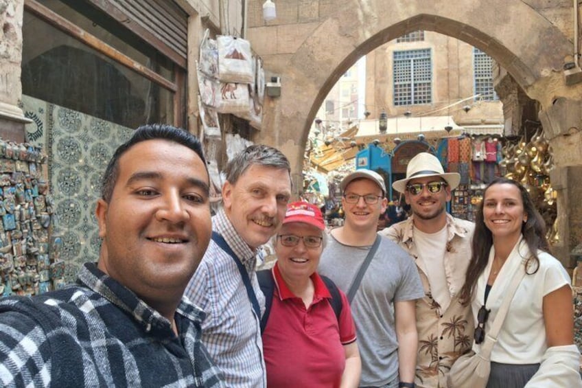A group of people in a narrow street with a stone archway, shops, and hanging ornaments. 3