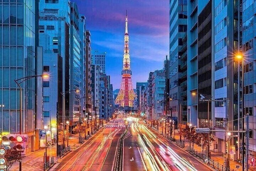 A city street with the Tokyo Tower illuminated, surrounded by modern buildings and busy traffic. 2
