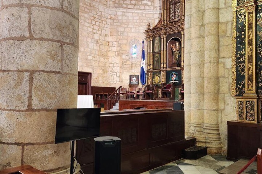 Een kerkinterieur met stenen muren, houten banken en een groot altaar met religieuze iconen. 2