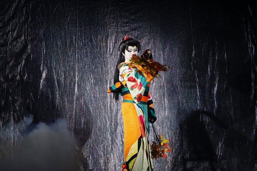 Eine Person in traditioneller Kleidung mit einem farbenprächtigen Kimono und einem Fächer vor einem Wasserfall. 2