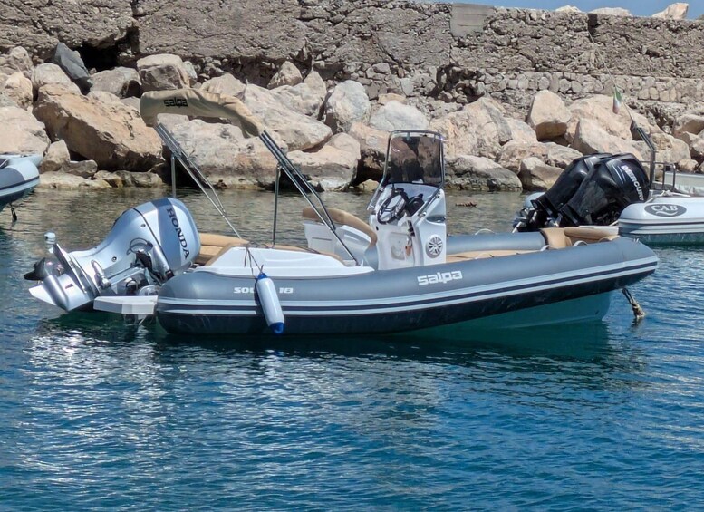 A small inflatable boat with an outboard motor, a canopy, and a life preserver, docked near rocky shores. 1