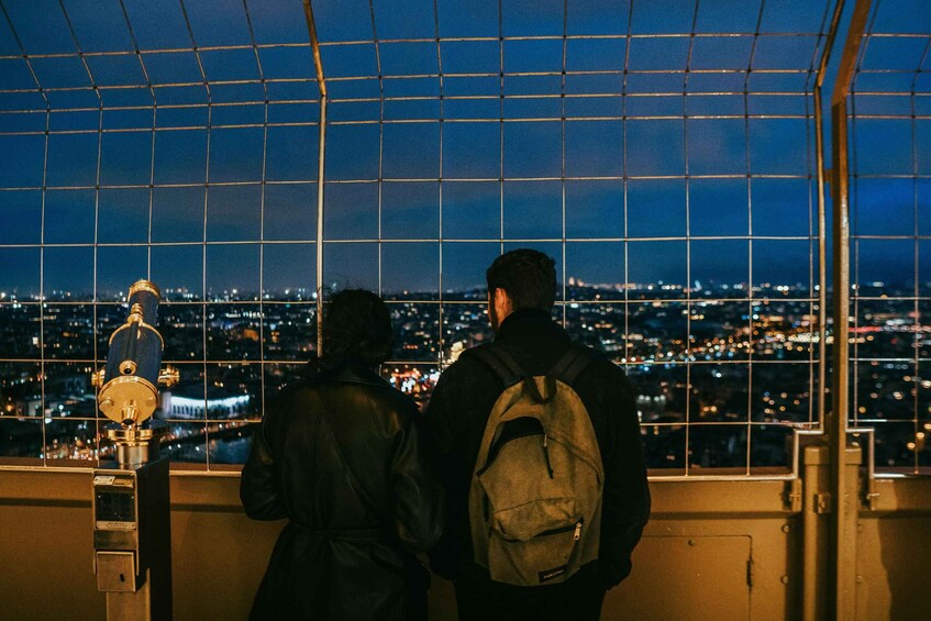 Two people standing by a window overlooking a cityscape at night. 5