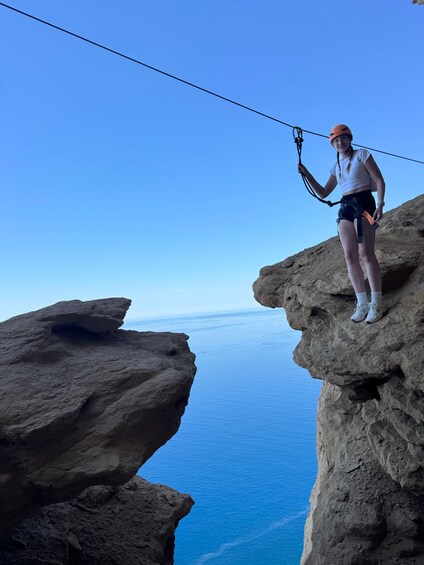 A person on a rock ledge with a rope, overlooking a vast body of water. 3