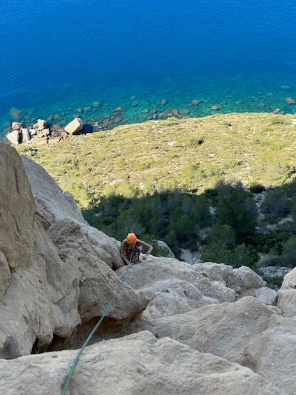 A person climbing a rocky slope with a clear view of the sea and a hilly landscape in the background. 5