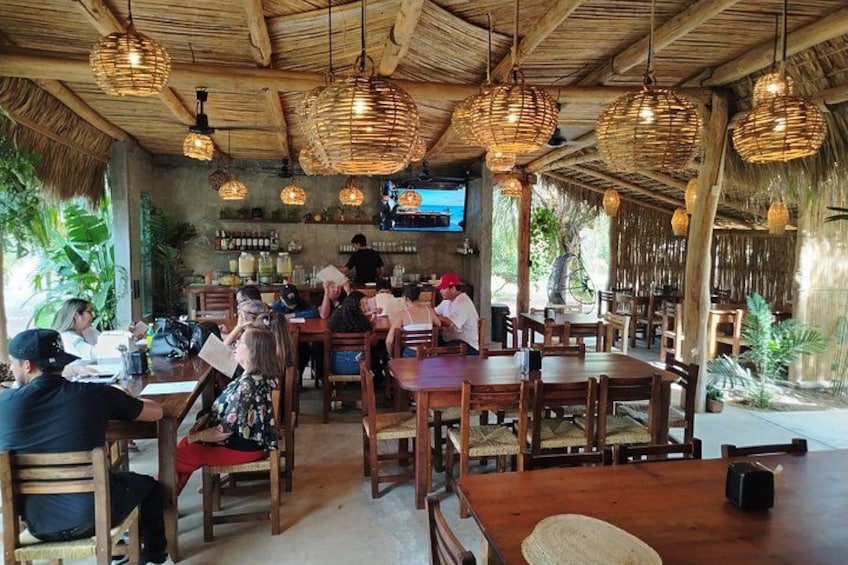 A restaurant with wooden tables and chairs, hanging wicker lamps, and a TV screen on the wall. 4