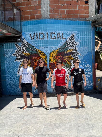 Four people standing in front of a colorful mural with the word "VIDEAL" on a blue wall. 1